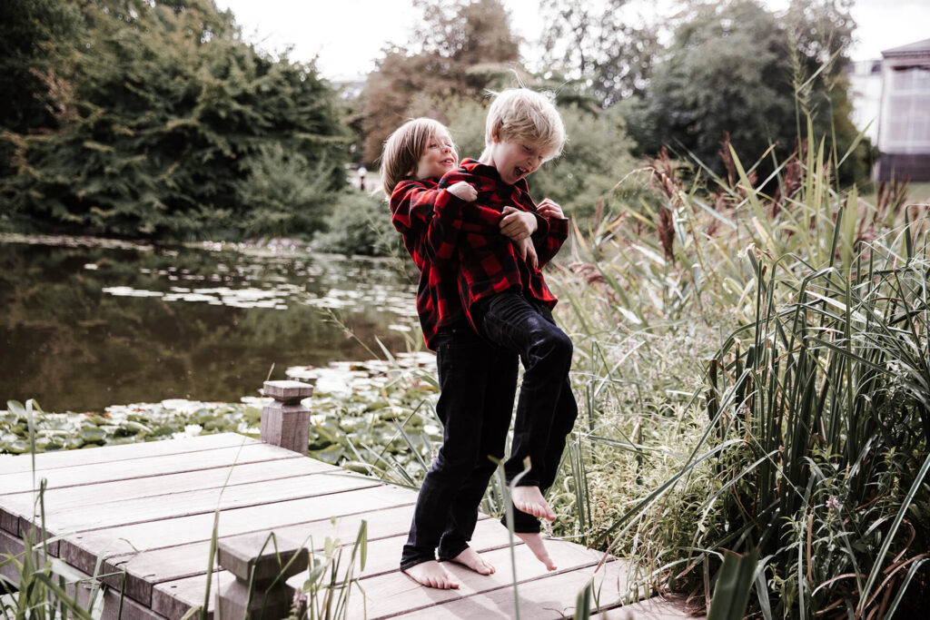 Братья играют и дурачатся на деревянном мостике у пруда