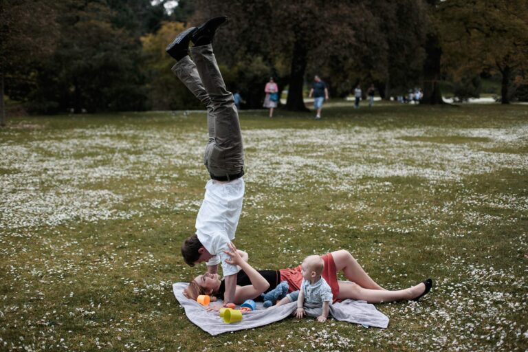 В парке на пледе: мужчина стоит на руках, рядом женщина и малыш