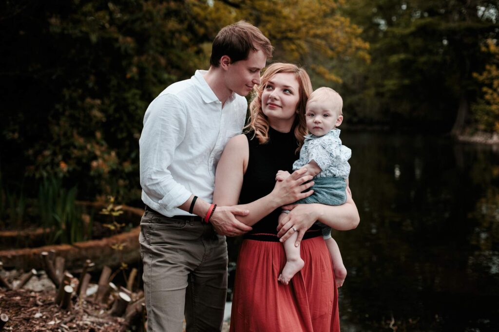 Семейная пара держит малыша на руках возле пруда