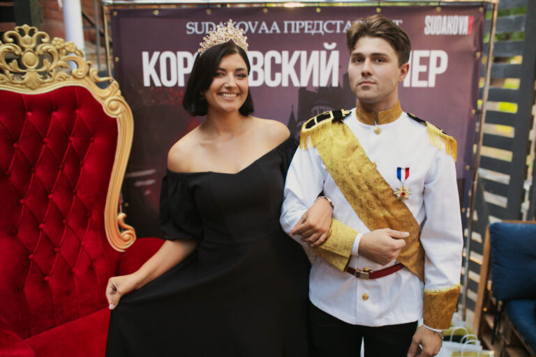 Гостья с короной и ведущий в белом мундире у баннера