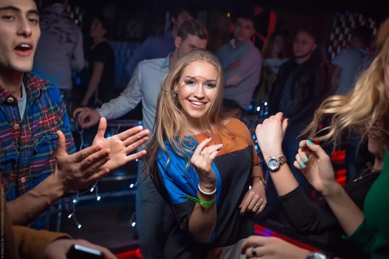 Гостья танцует среди друзей в клубе, вспышка на тёмном танцполе