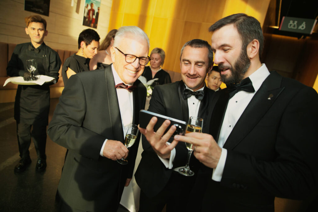 Участники вечера в смокингах просматривают фотографии на телефоне