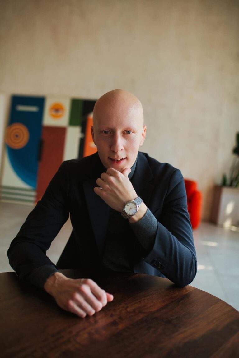 Сидит за столом, подбородок на руке