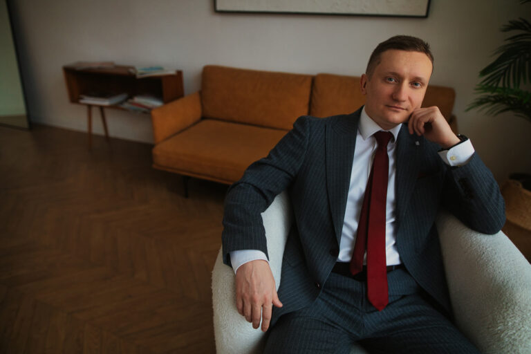 Сидит в белом кресле в костюме