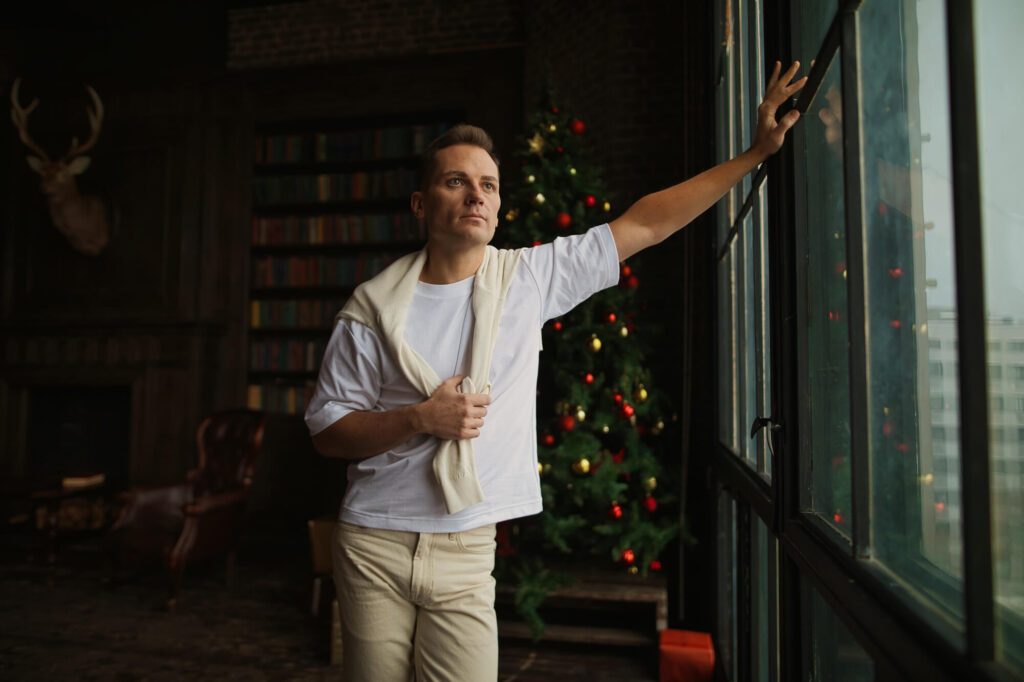 Мужчина у окна с праздничной елкой на фоне