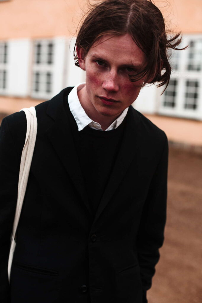 Молодой человек в черном костюме на фоне здания