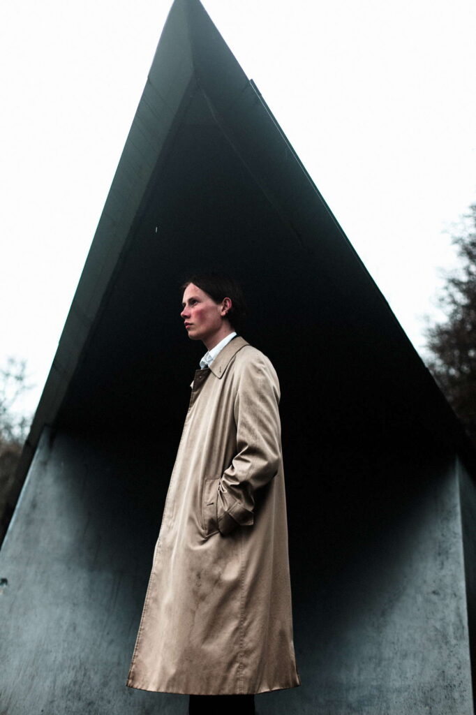 Молодой человек в пальто у архитектурного сооружения